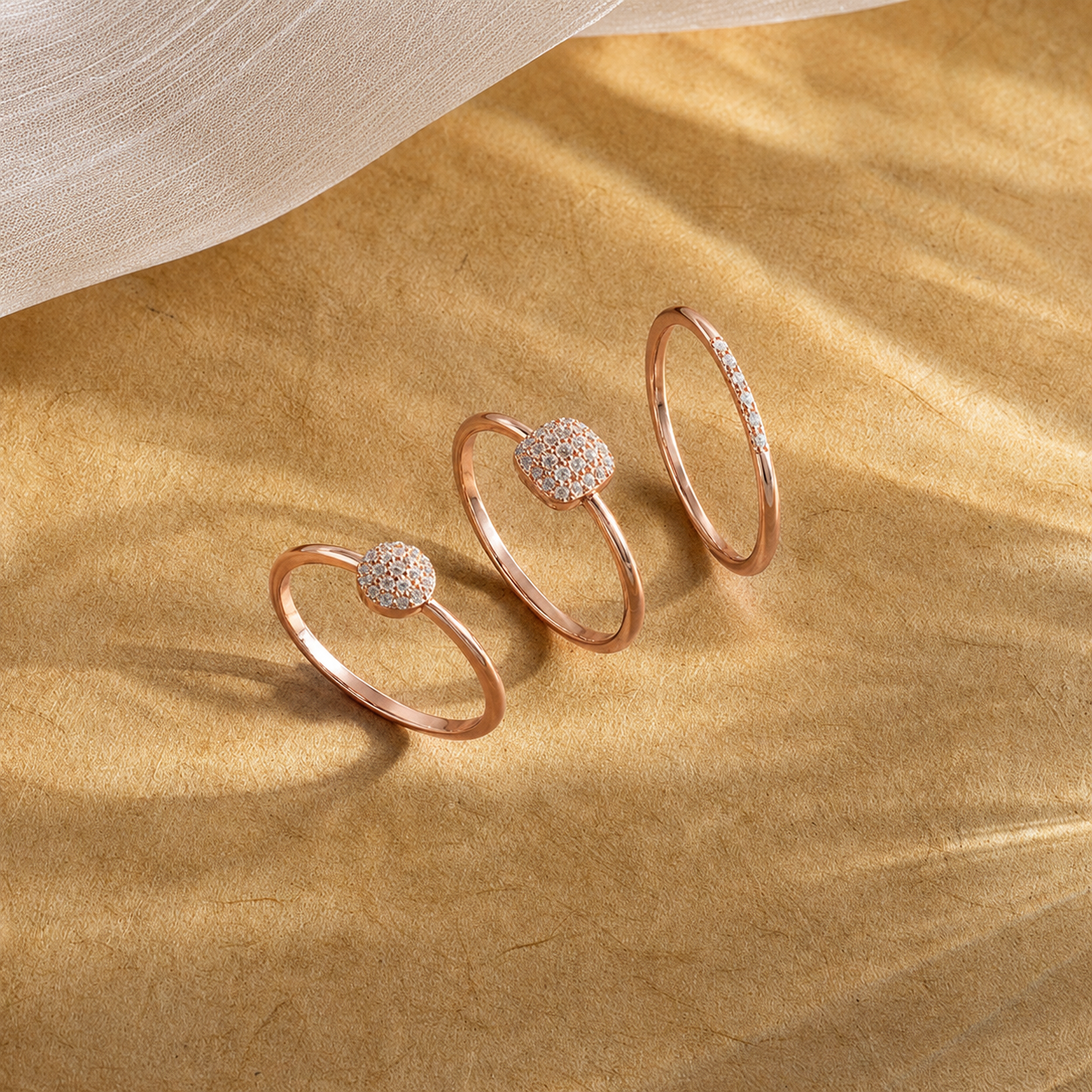 Three rose gold rings with diamond accents on a beige fabric background